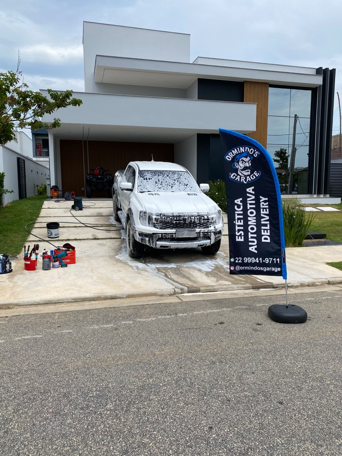 Pickup em lavagem com espuma na garagem de casa, ao lado da bandeira Ormindo's Garage